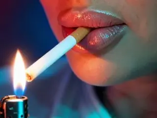 Close-up of a woman with glossy lips lighting a cigarette with a lighter in moody neon blue lighting.