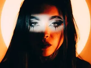 LaurenRousex looks directly at the camera with a dramatic, high-contrast light masking her eyes, showing her dark hair and facial features.