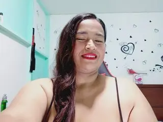 Laurita_RinconBusty poses with long dark hair, wearing a black bra or camisole top in a room with light-colored walls.