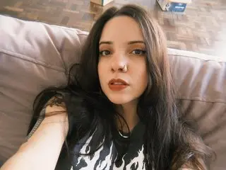 Young woman with long dark hair wearing a black graphic flame t-shirt relaxing on a grey sofa.
