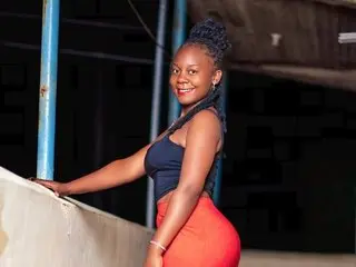 Smiling young woman in a black crop top and orange skirt posing outdoors at night.
