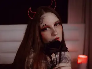 LeanaaKorale poses with a dark rose held near her mouth, wearing a black lace top and a thin headband with red horns.