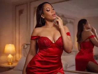 LeiaKesh poses in a red satin corset top, showing off her cleavage and shoulders against a soft indoor background.
