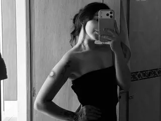 Black and white selfie of a tattooed woman in a black strapless top posing in a bathroom mirror.