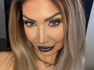 Lettie_Looner poses with a direct gaze, showing her long blonde hair and heavy eye makeup with thick lashes.