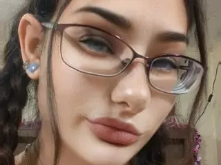 Close-up portrait of a young woman with braided hair and glasses looking at the camera with a soft expression.