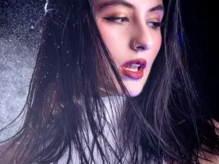 Glamorous woman with wet hair and bold makeup posing in a dark, shimmering glitter setting.