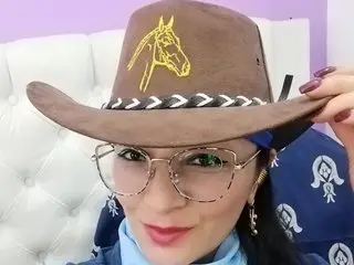 Lexygatamature wearing a brown cowboy hat with a gold horse logo and glasses, smiling at the camera.