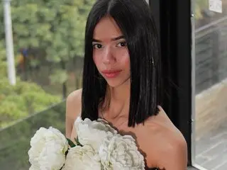 Young woman with long black hair holding a white flower bouquet in a bright outdoor setting.