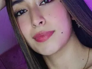 Close-up portrait of a young woman with long brown hair and pink makeup in soft purple lighting.