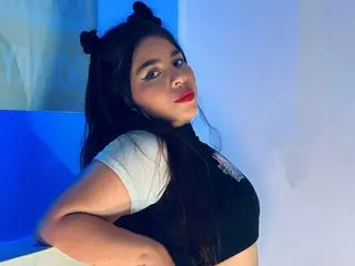 LianyTaylor poses with long dark hair, wearing a black and white top against a blue and white background.