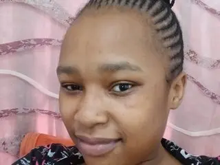 Smiling young woman with braided hair wearing a patterned black top in a bright indoor setting.