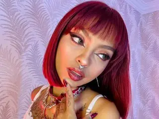 LiilithNyx poses with a direct gaze, showing her red hair and nose ring while wearing a white lace top.