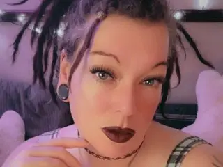 LilithLaneXx looks into the camera wearing a black choker and a plaid top, with her dark hair styled in dreadlocks.