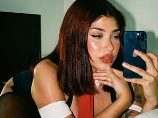 LilithOwens takes a mirror selfie wearing a red top, looking into her phone with her hand on her chin.