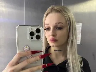 Lilith_Noir21 poses with long red nails, wearing a black top and a black choker, with her long blonde hair down.