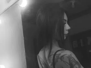 Side profile of a tattooed woman with long dark hair in a moody, dimly lit indoor setting.