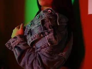Young woman in a denim jacket posing under moody red and green neon lights.