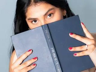 LinnaValenciia holds a dark blue book up to her face, partially obscuring her eyes and long dark hair.