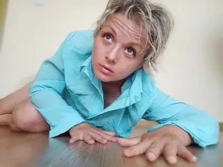LinsyKim lies on her stomach on a wooden floor, wearing an unbuttoned light blue shirt and looking up at the camera.