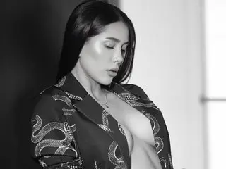 LisWalton poses with long dark hair, wearing an open dark patterned shirt that exposes her bare breasts.