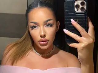 Glamorous woman in a pink top and diamond choker taking a selfie in a moody indoor setting.