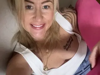 LittleMissSweetLips smiles while wearing a white tank top that shows off her cleavage and chest.