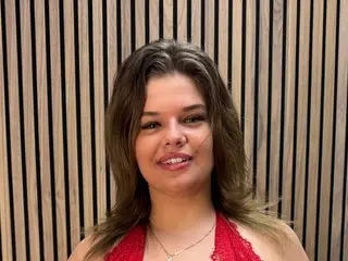Smiling young woman in a red lace dress posing against a modern vertical wood slat wall background.