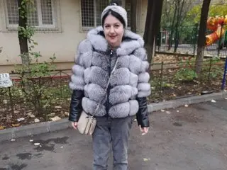 Woman in a grey faux fur hooded jacket and beanie standing outdoors on a fall day.