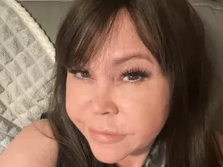 Lolly_coxx smiles for a close-up selfie while laying back against a white textured pillow.