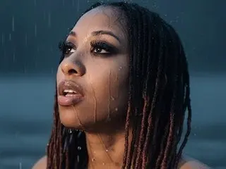 LondonSquirts looks toward the camera with an open mouth, showing her dark hair and facial features against a dark background.
