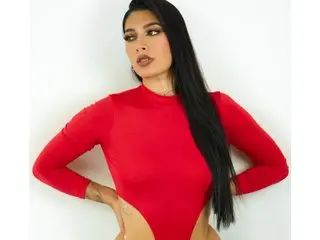 Louanebouroff poses in a red long-sleeved bodysuit, showing her long black hair and cleavage against a white background.