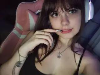 LoveluKristi poses with her hand near her mouth, showing her long dark hair and black tank top in a dimly lit room.