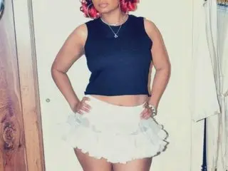 LovelyLavender22 poses in a black tank top and white ruffled mini skirt, showing off her hair and waist.