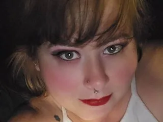 LovenseLexi90 with red lipstick and bangs looks into the camera while wearing a white tank top.