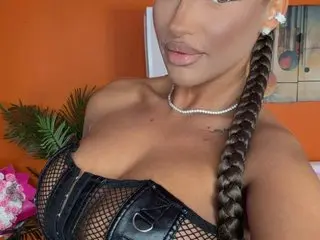 Glamorous woman in black mesh corset and pearl necklace with long braided hair against an orange background.