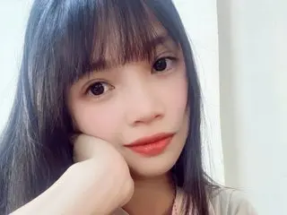 Portrait of a young woman with long black hair and bangs smiling softly in a bright indoor setting.