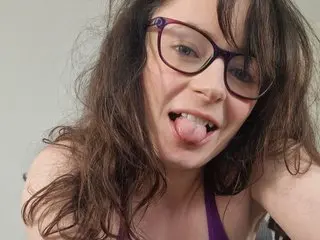 Smiling woman with brown hair and purple glasses wearing a purple tank top in a bright indoor setting.