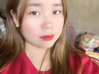 Luciibae poses with long brown hair and red lipstick, wearing a red top against a soft-focus background.
