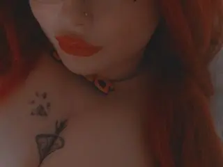 LucinderLush shows her neck and chest, featuring a black choker and a heart-shaped tattoo on her skin.