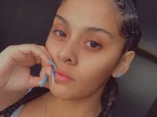 LuckyFreakk poses close-up, showing her face and dark hair styled in braids, looking directly at the camera with a soft expression.