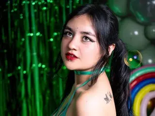 Young woman with dark hair and red lipstick wearing a green choker against a vibrant green balloon backdrop.