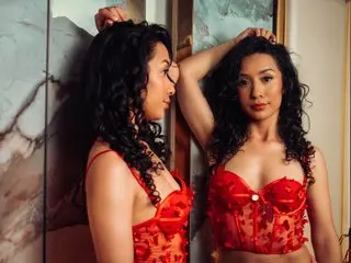 Beautiful woman with curly hair in red lace lingerie posing against a marble wall in a moody setting.