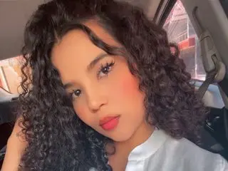 Luna_Monroe poses with a close-up headshot, showing her long, dark curly hair and light makeup against a soft indoor background.