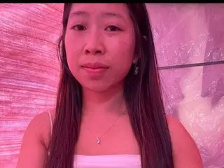 Luna_lovee poses with long dark hair, wearing a white top against a soft pink background.