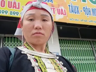 Vietnamese woman in traditional ethnic attire and silver jewelry standing outdoors in front of a storefront.