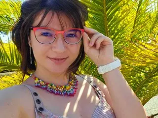 LyzMania poses outdoors in sunlight, wearing a patterned purple bra and red glasses with her dark hair down.