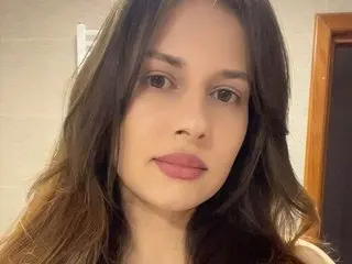 MEERA19 poses with a close-up headshot, showing her long dark hair and face against a neutral indoor background.
