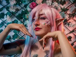 MEIJAISENN poses with her hands near her face, showing her long pink hair and red lipstick in a floral setting.