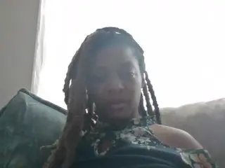 MEOWKittyKattMEOW poses in a dark patterned top with her long brown dreadlocks falling over her shoulders.